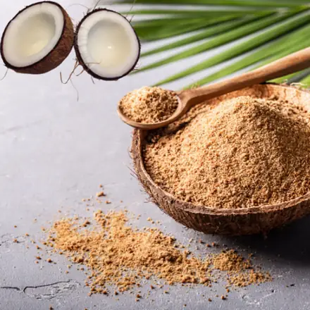 Coconut jaggery in a coconut shell bowl beside halved coconuts